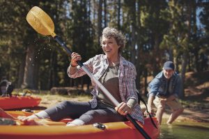 Portrait of happy senior paddling kayak in the lake with man supporting from behind. Mature couple enjoying a day at the lake.